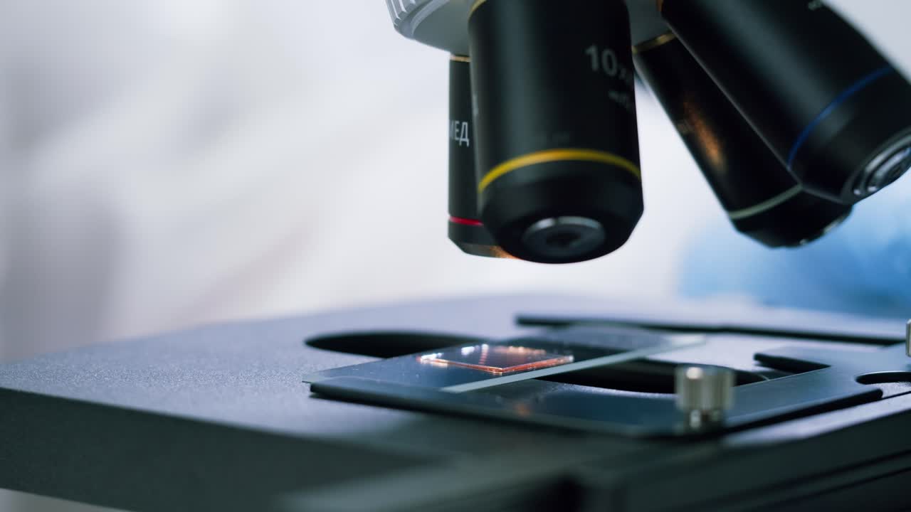 Close-up of Hand in Glove Placing Sample Slide Under Microscope