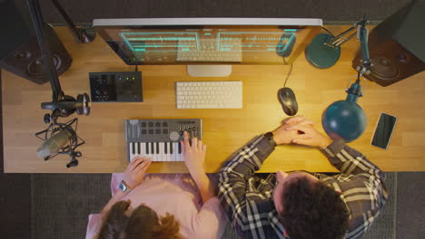 overhead view of male and female musicians at computer with keyboard in studio at night