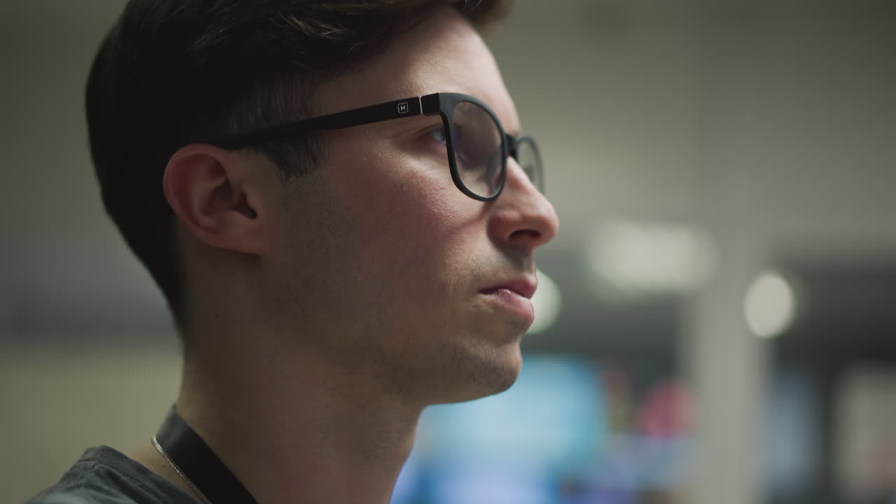 Profile of television control room operator wearing glasses, focused on monitors and controls, managing broadcast tasks, behind a studio control panel, in professional media environment