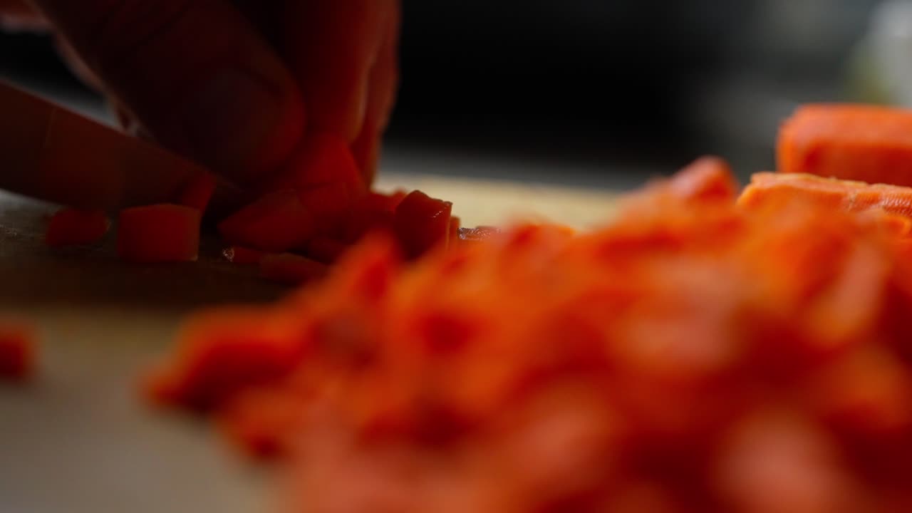 Vegetable Chef slices carrots thinly with knife on soft lit kitchen top