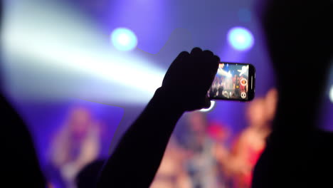 spectator capturing a live music concert with a smartphone camera, surrounded by vibrant stage lights and an enthusiastic crowd, creating an electrifying atmosphere filled with energy