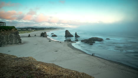 tourist sightseeing through splashing sea waves with stacks at the ocean under foggy sky