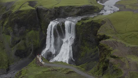 turistas viendo la cascada de agua escénica en la asombrosa cascada de fagrifoss en el sureste de islandia - drone aéreo - tiro de retroceso