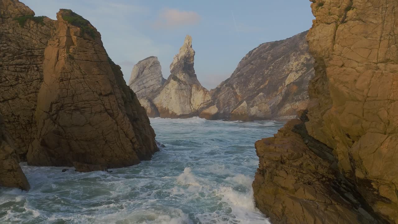 Rough sea on a remote sand beach surrounded by cliffs at sunset