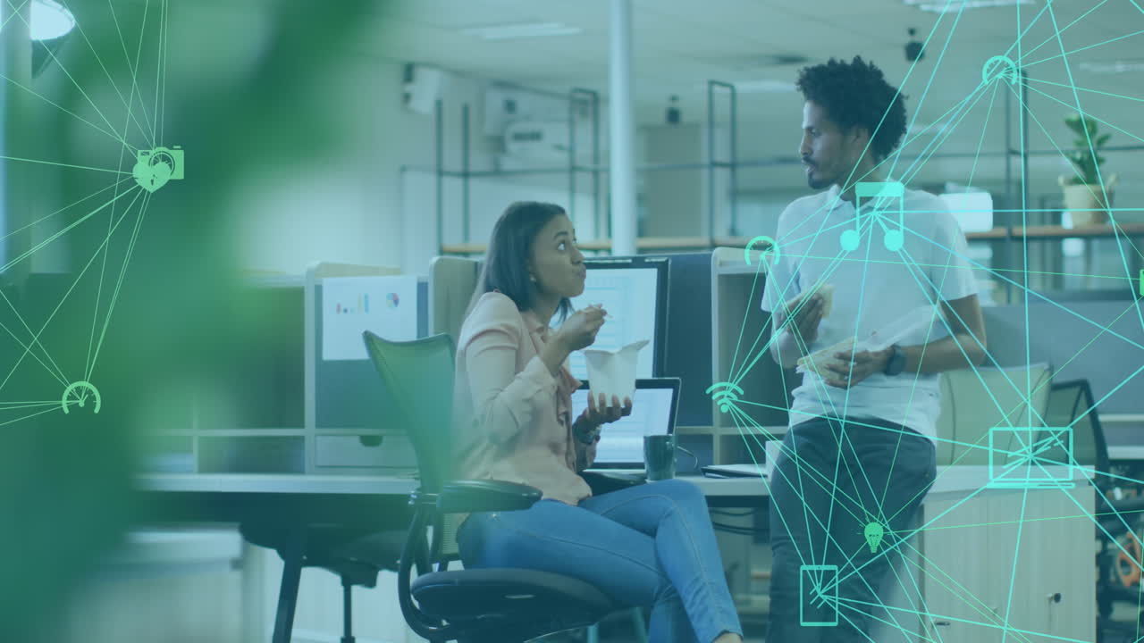 Animation of globes of digital icons spinning over diverse man and woman having snack at office