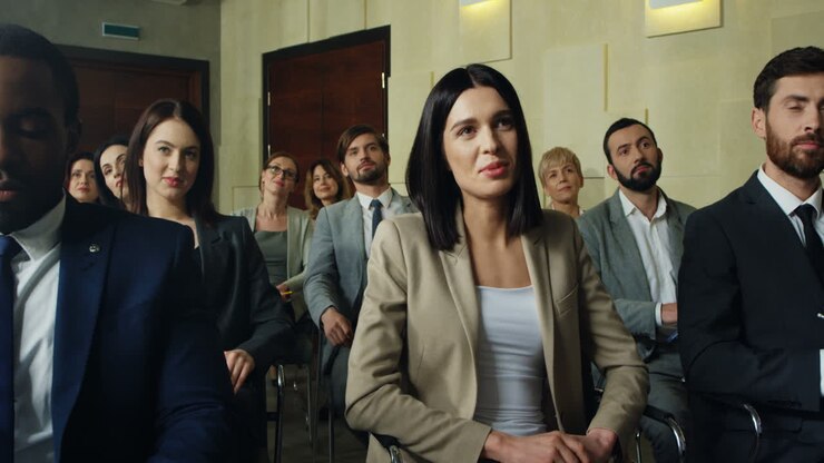 Close-up view of the audience at a business conference listening to the speaker, then caucasian businesswoman rises her hand and asks a question