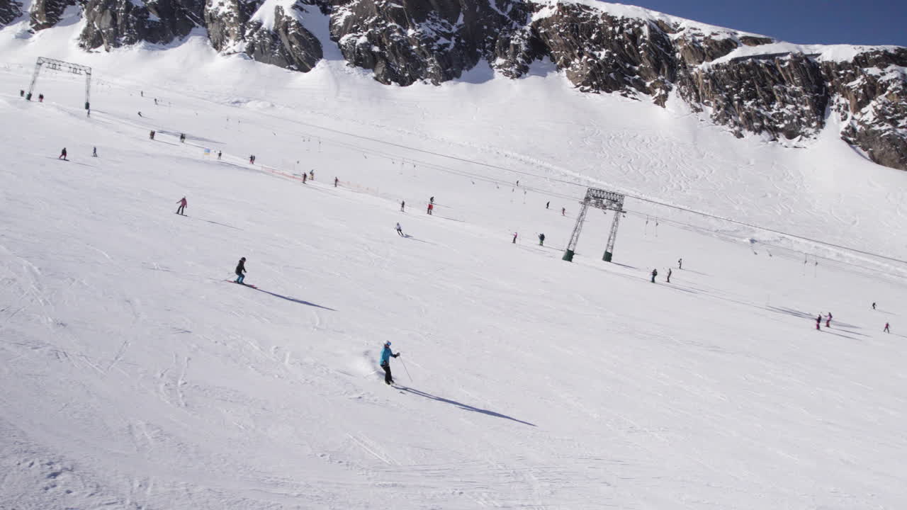 Tilting down drone shot of people skiing on ski slope on snowy kitzsteinhorn mountain in austria on sunny day
