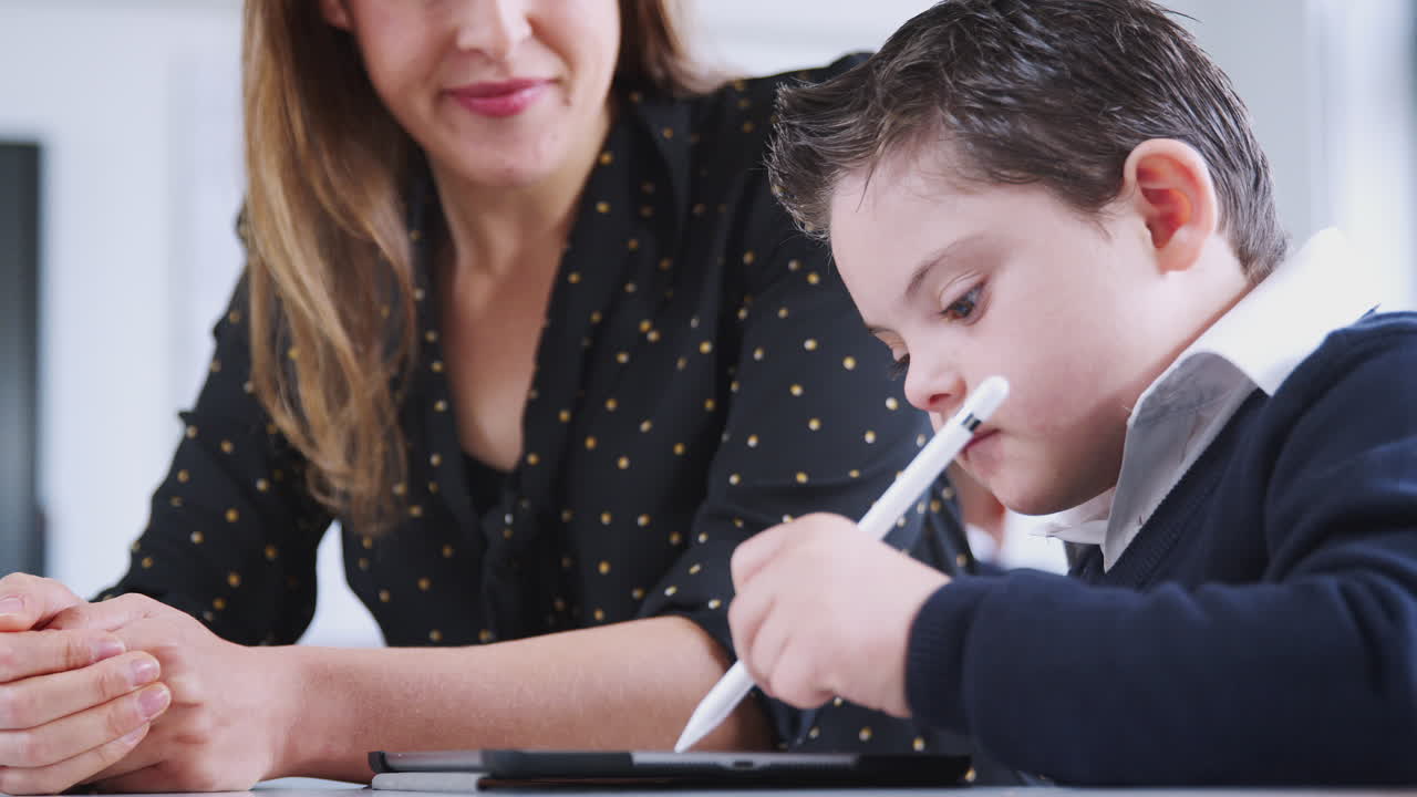 maestra trabajando con un niño con síndrome de down usando una tableta en la escuela primaria, ángulo bajo, de cerca