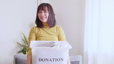 portrait of young asian woman looking at camera holding box with clothes for donation