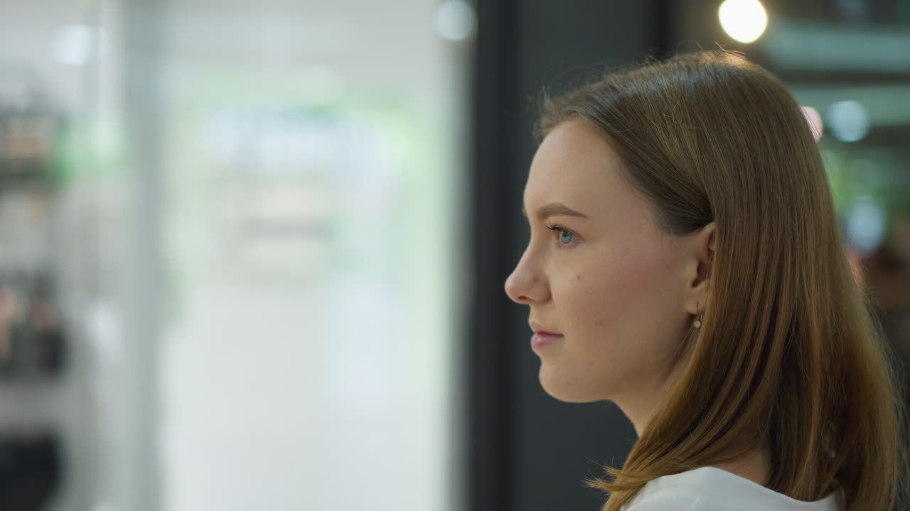 una joven está de pie frente a una tienda de ropa en un centro comercial observando un maniquí vestido con pantalones y sostén, con un fondo borroso con estantes de ropa, otros compradores y exhibiciones brillantes en una tienda moderna
