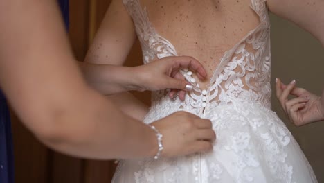 portrait back shot of bride´s mother helping to button up bride's elegant white weding dress,