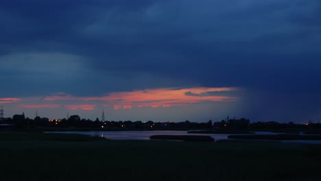 time lapse of dramatic dark thunderstorm clouds with lightning strikes rolling over the city and lake liepaja after the sunset, wide shot