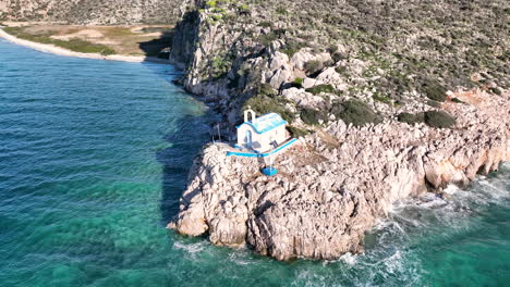 drone footage of a small greek orthodox church on the rock next to the sea