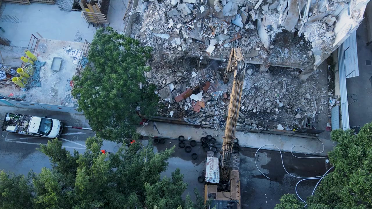 Vista aérea de drone de trabalho de demolição com pulverização de água para controle de poeira em projeto de renovação urbana na Rua David, פינוי בינוי, תמא 38, redesenvolvimento e transformação da cidade.