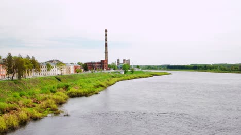 still waters and wide skies frame the industrial edge of a baltic town. tall chimney and green banks. shot in daugavpils, latvia, baltics