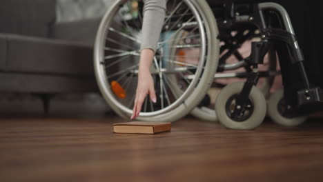 mujer se mueve en silla de ruedas tratando de alcanzar el libro en el suelo