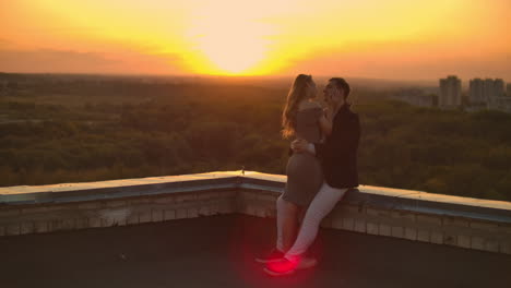 abbracciarsi in piedi sul tetto al tramonto. tetto d'estate al tramonte. un uomo con una ragazza è venuto a un appuntamento romantico sul tetto.