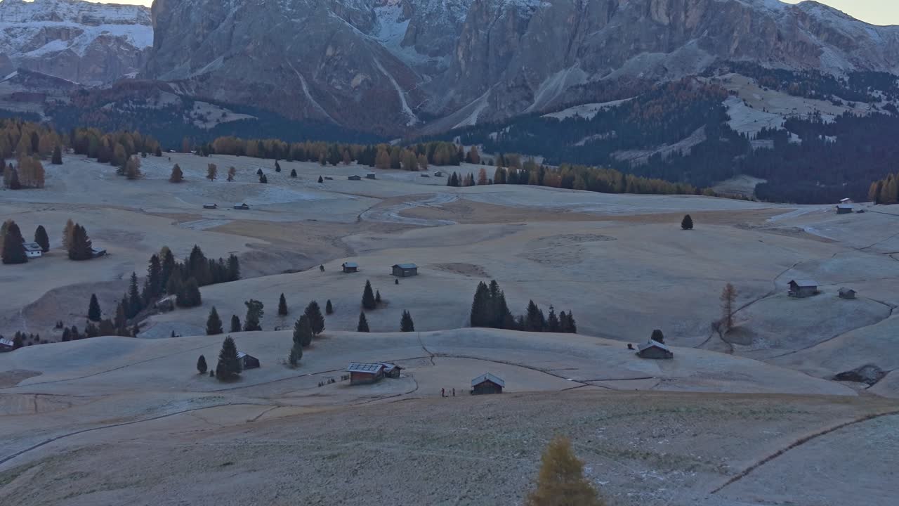 Alpe di Siusi con colori autunnali, baite in legno e alberi su un prato erboso