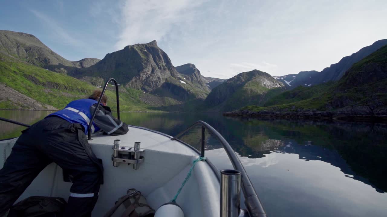 hombre en la proa del barco flotando en el lago cristalino junto a las montañas rocosas durante el día en noruega