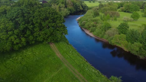 Aerial-drone-video-of-scenic-British-countryside-with-green-fields,-trees-and-bright-blue-river-in-summertime---Rickerby-Park,-Carlisle,-UK