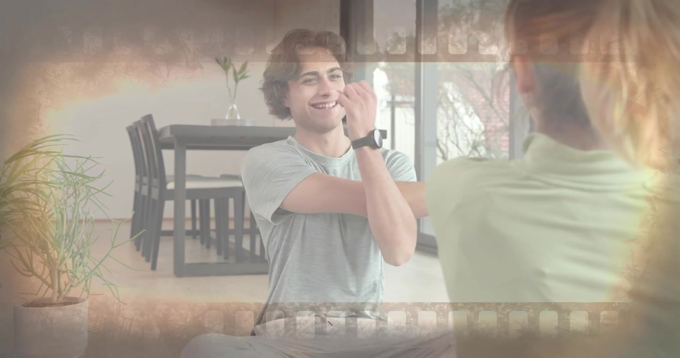 Woman initiating cross-body shoulder stretch on hardwood floor, inspiring man mirroring for fitness