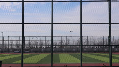 timelapse of people walking in soccer field seen through sports netting fence.