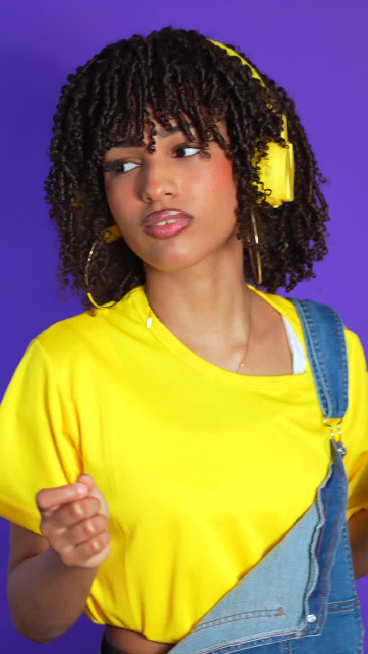 Woman with headphones and yellow shirt dancing on purple background