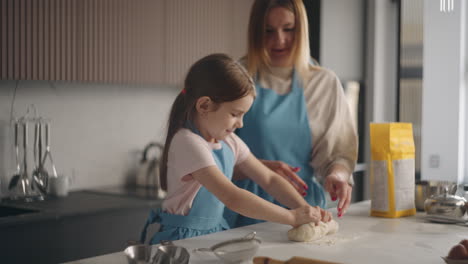 housewife and little daughter are making dough for bread in home together mother is kneading pastry