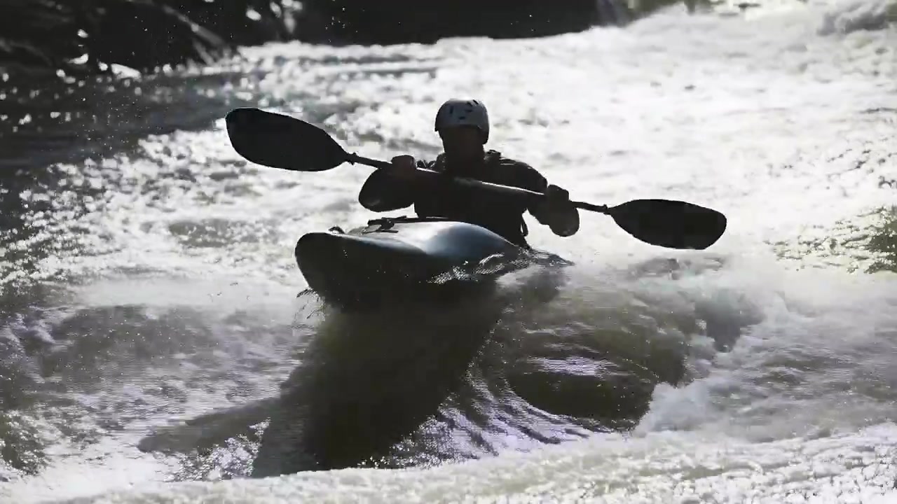 Kayaker che pagaia controcorrente, remando tra le rapide per mantenere l'equilibrio, indossando un casco.