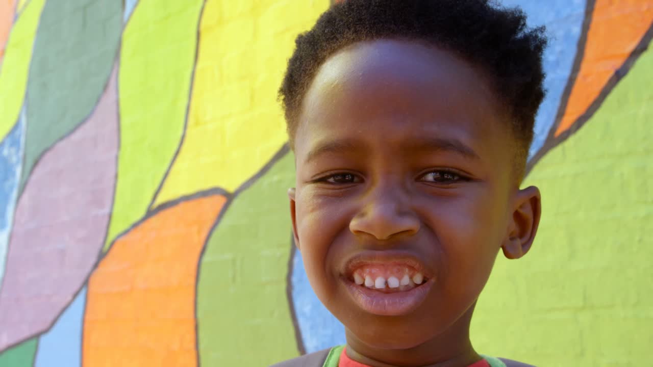 Front view of happy African American schoolboy standing against wall in school 4k