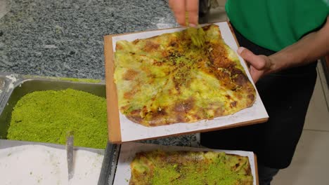 chef sprinkles pistachio powder on the top of the freshly baked katmer dessert