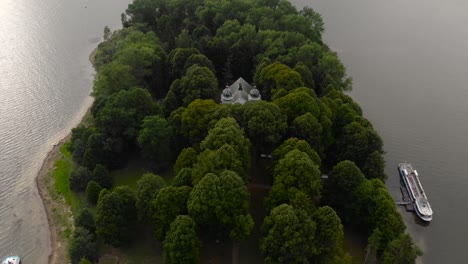 backwards aerial tilt up from church in between trees on slanicky art island in orava, slovakia