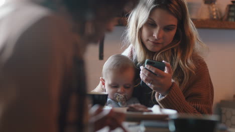 Madre-Joven-Con-Bebé-En-La-Cafetería-Usando-Un-Teléfono-Inteligente-Tomando-Café-Relajándose-En-Un-Restaurante-Concurrido-Disfrutando-De-La-Maternidad