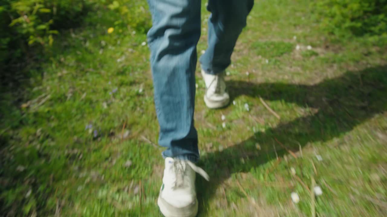 Man's feet step through grassy meadow with scattered white flowers, walking through nature, low angle walking
