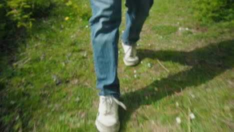 man's feet step through grassy meadow with scattered white flowers, walking through nature, low angle walking