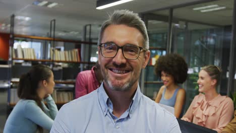 Portrait-of-caucasian-businessman-smiling-over-diverse-business-colleagues-talking