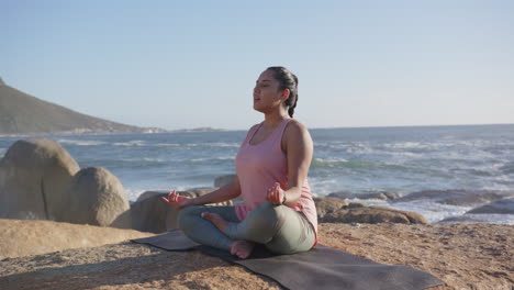 practicing mindfulness by ocean, asian woman meditating on yoga mat, copy space