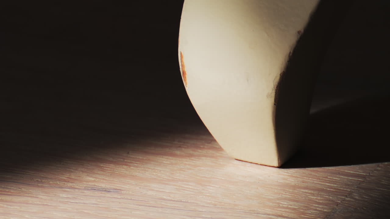 Primo piano di una scultura minimale e ricurva illuminata dalla luce solare, che crea ombre morbide su una superficie