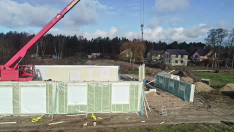 vista aérea de un sitio de construcción con una grúa roja levantando paneles de pared bajo un cielo despejado
