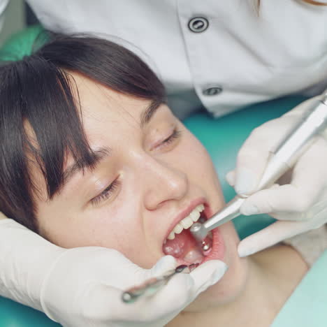 Young woman on the procedure of removing deposits on the teeth. A dentist uses special tool for a cleaning . Close-up.