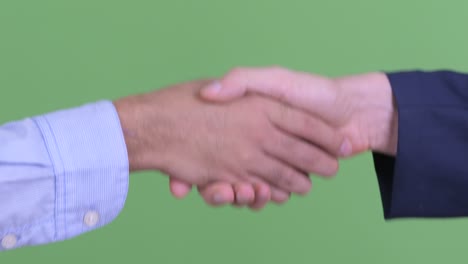 two businessman having handshake against green studio background