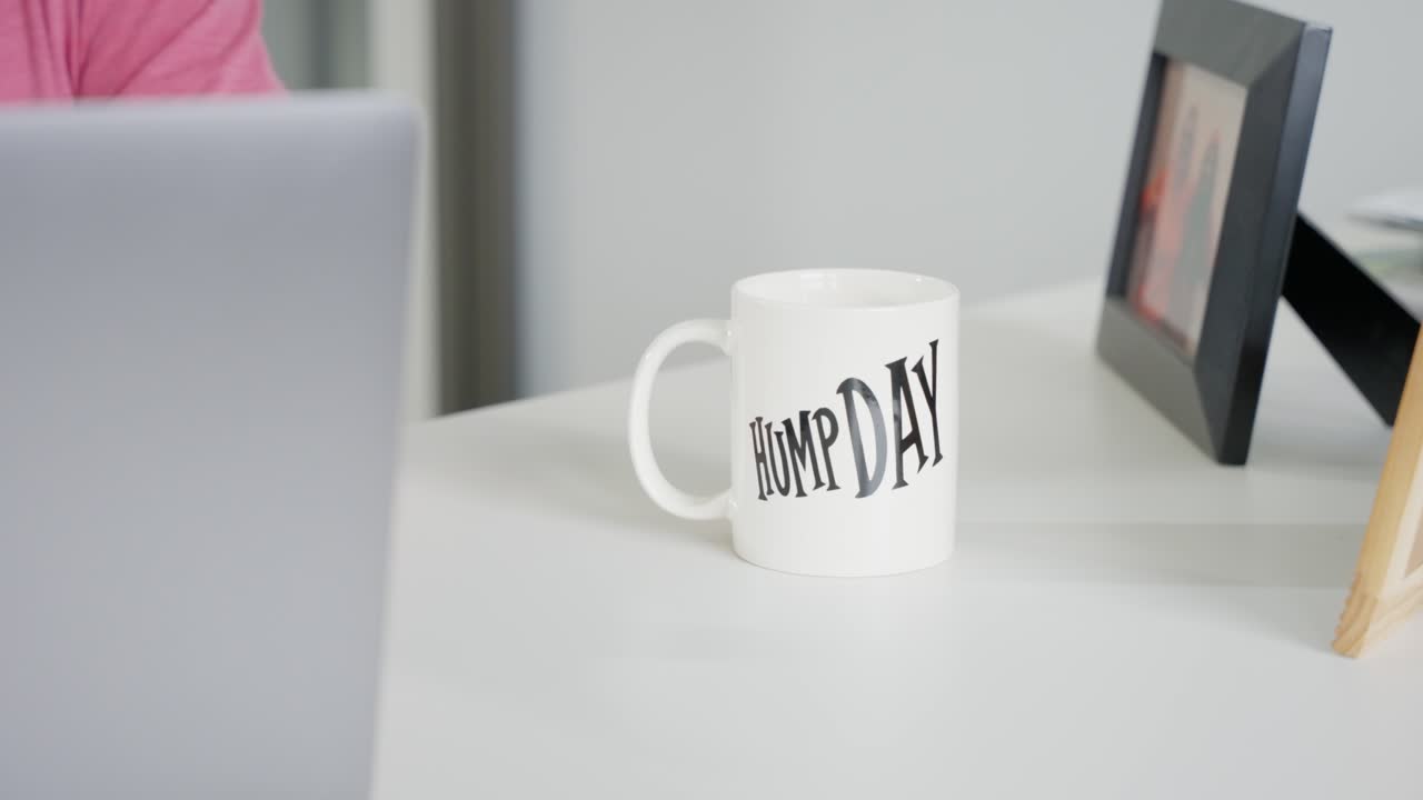 taza de vidrio con impresión del día de la joroba en la mesa de oficina blanca, lugar de trabajo con empleado en la computadora portátil