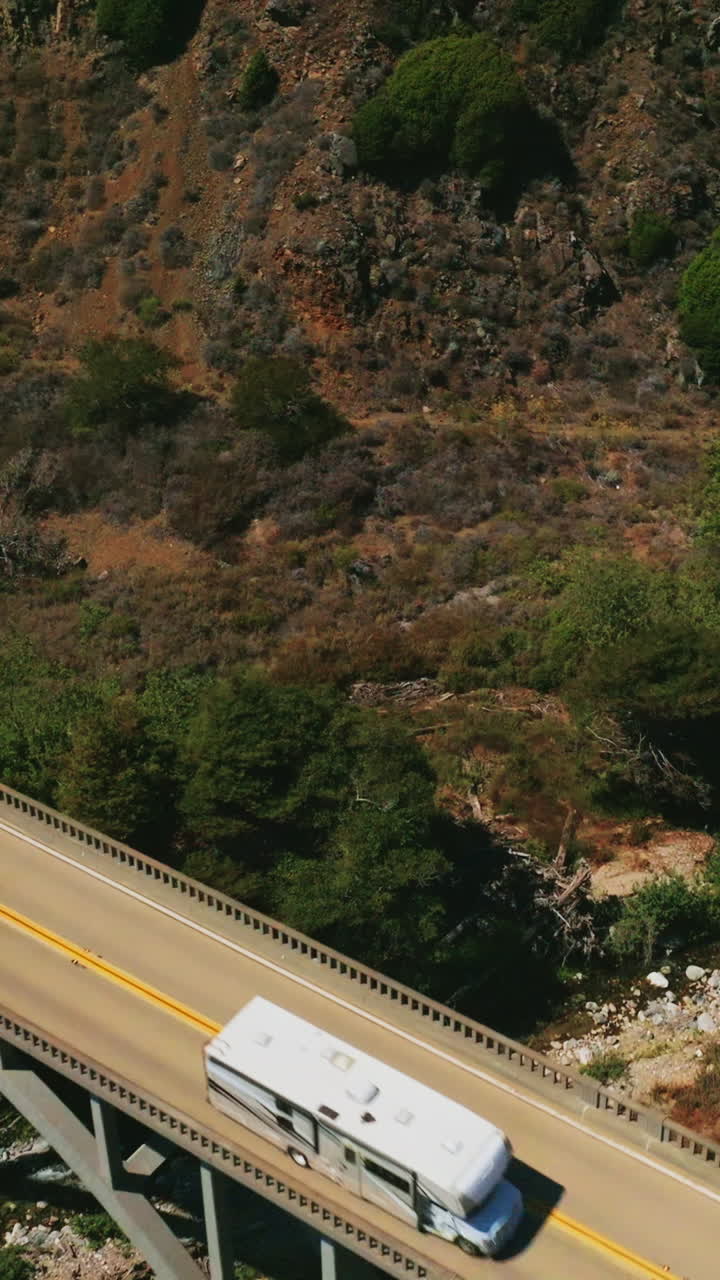 Bridge with cars moving by. Arched bridge in the mountains above the little creek. Aerial view. Vertical video