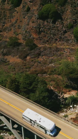 bridge with cars moving by. arched bridge in the mountains above the little creek. aerial view. vertical video