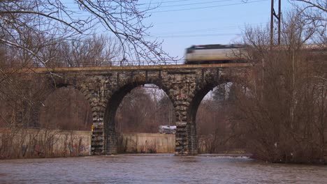 un tren de pasajeros pasa por un viejo puente de piedra