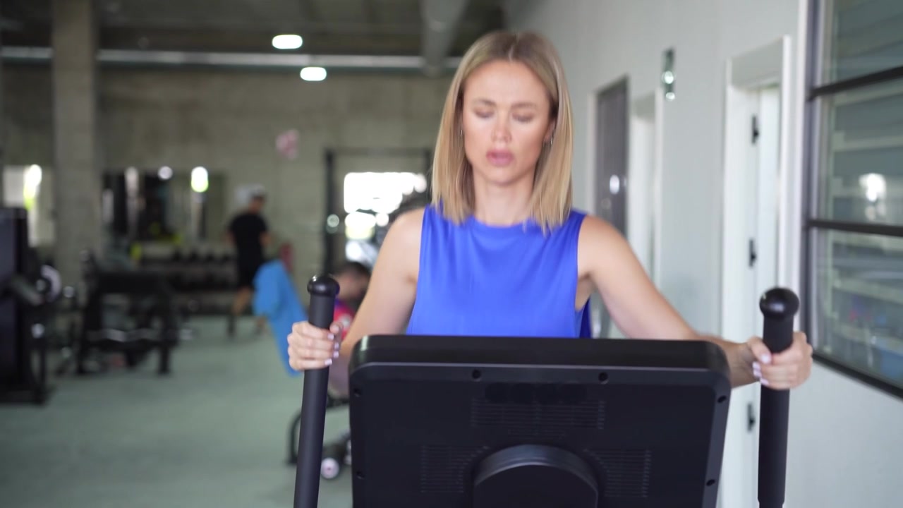 Una donna sta svolgendo una sessione di allenamento su una macchina ellittica in un centro fitness moderno.