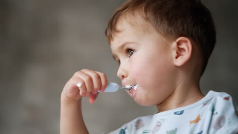 lovely little boy taking a full spoon of dairy to his mouth. low angle view on the toddler eating yogurt.