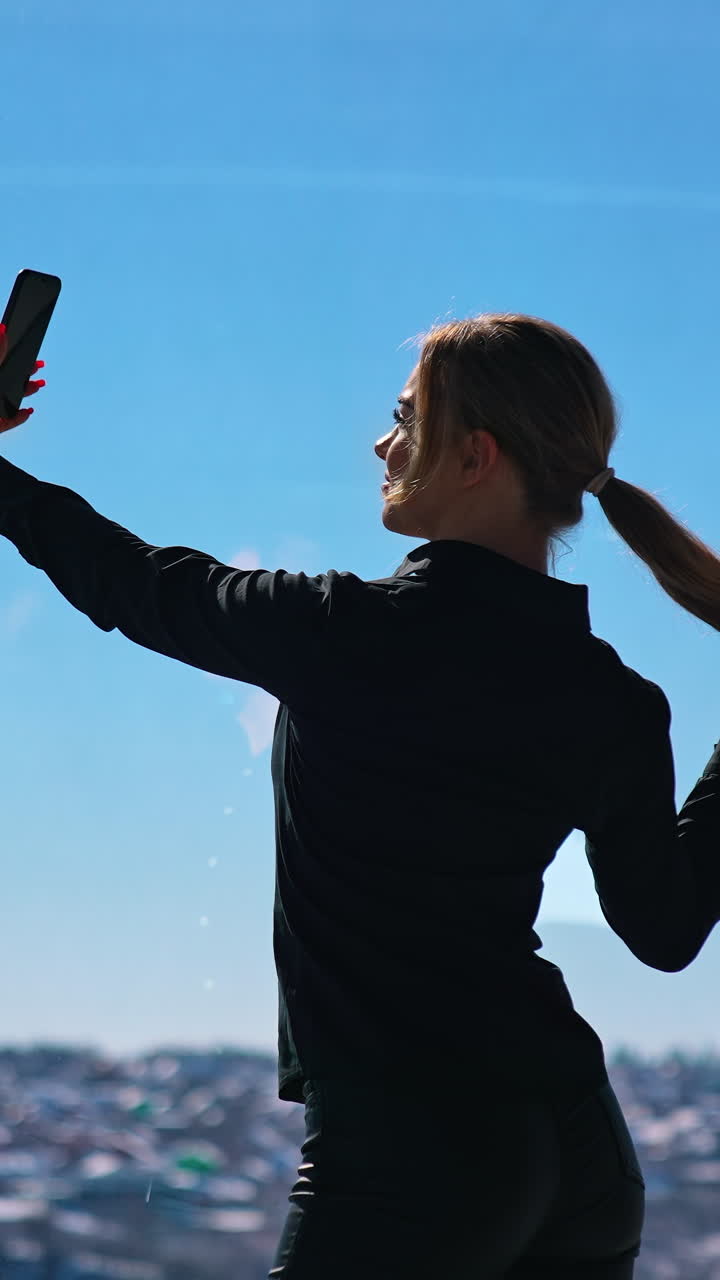 Lovely business woman in black taking photo of herself. Beautiful young woman doing selfie on smartphone while standing at office window. Vertical video