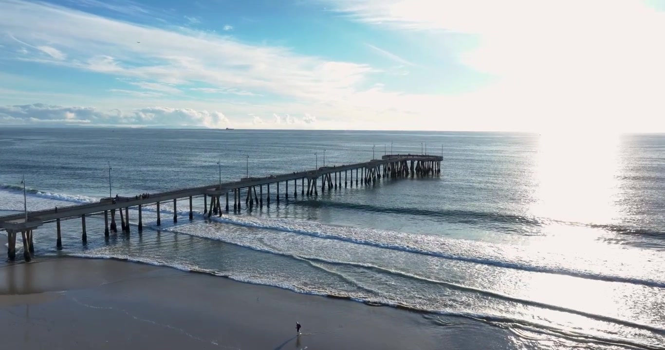 Una ripresa aerea cinematografica grandangolare con drone che ruota lentamente in avanti sopra il molo di Santa Monica, che si protende da Venice Beach, al largo della costa del Pacifico a Los Angeles, California.