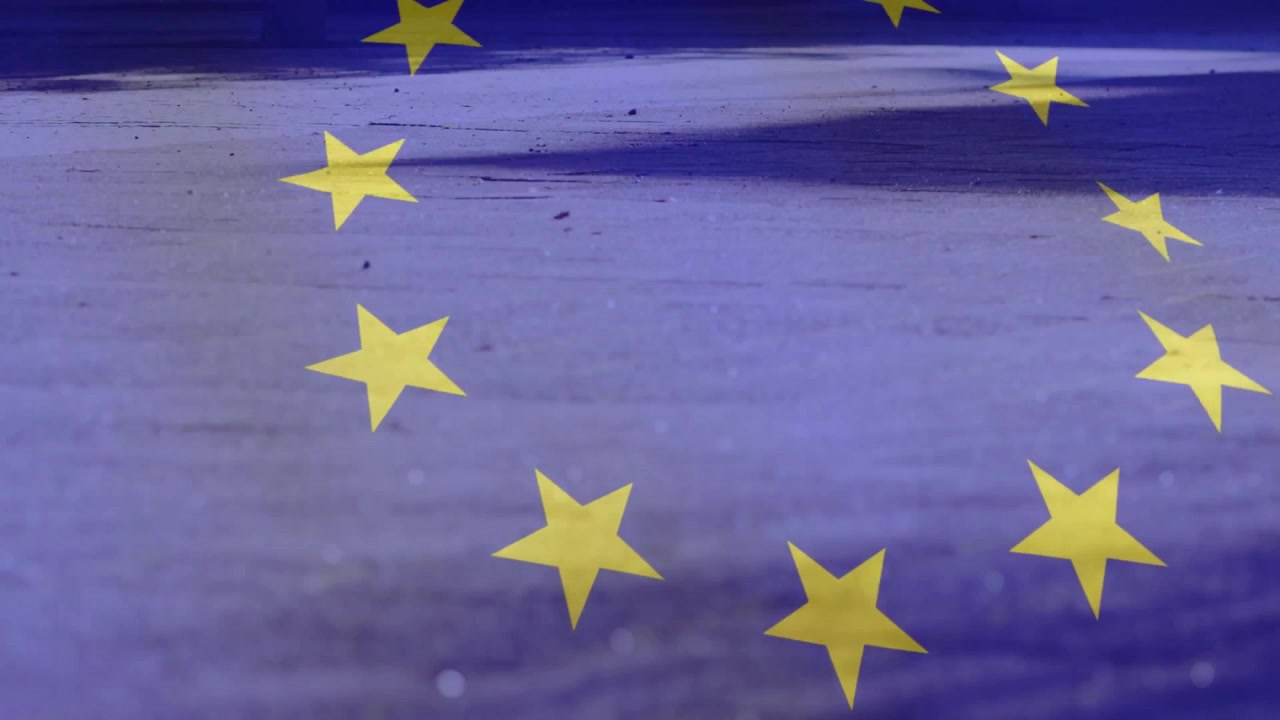 Luce solare bassa che illumina le stelle dell'UE che fluttuano sul cemento, poi una donna che avanza portando una borsa della spesa rossa.